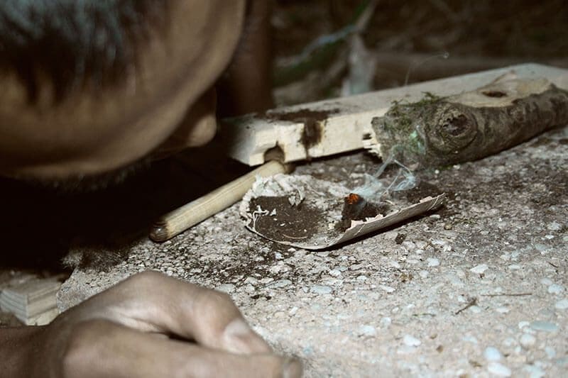 Ein angehender Wildnisexperte bläst die erste Glut nach dem Feuerbohren an. Feuermachen wird im Wildniscamp beim Leben in der Wildnis zu einer täglichen Routine.