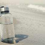 Eine Trinkflasche aus Glas steckt im Sand fest