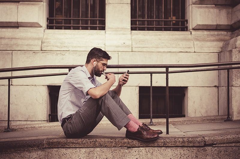 Mann sitzt auf einer Laderampe und hört sich einen unserer Blogartikel auf seinem Smartphone mit ReadSpeaker an.