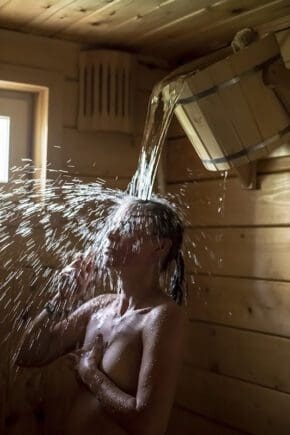 Frau übergießt sich nach einem Saunagang mit eiskaltem Wasser