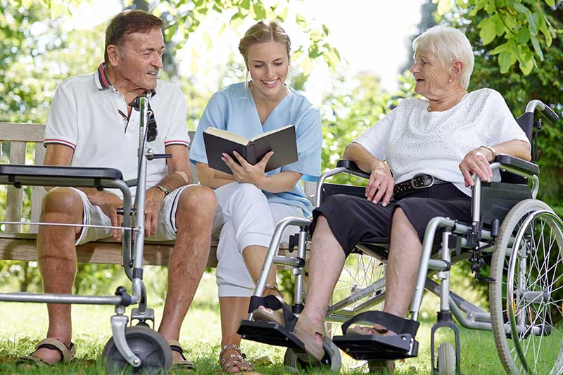 Pflegerin liest Rentnern aus einem Buch vor