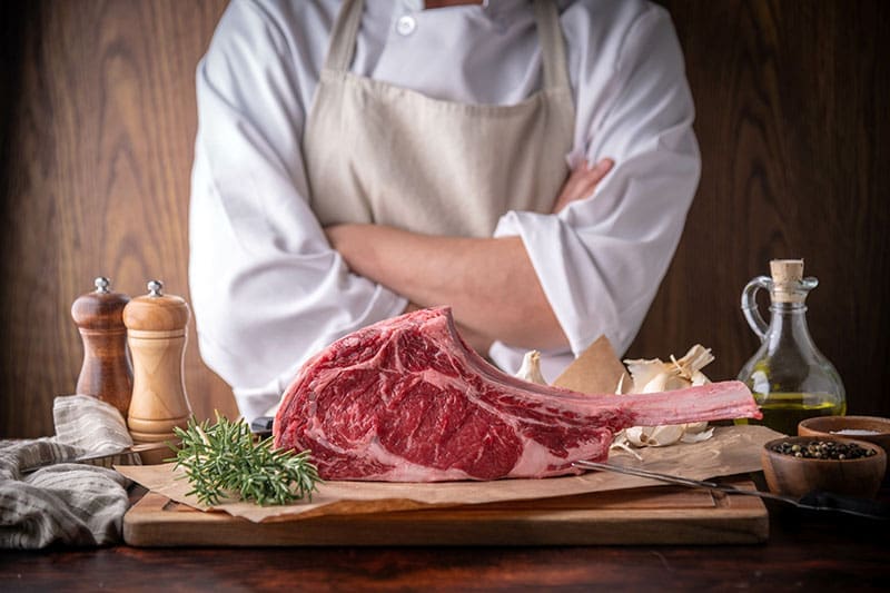 Koch zeigt rohes Fleisch am Knochen